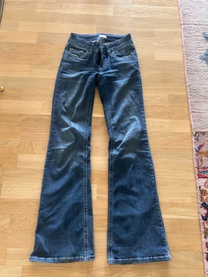 Blå bootcut jeans med broderade fickor - Snygga blå bootcut jeans med klassisk femficksdesign och broderade detaljer på bakfickorna. Jeansen har låg midja och är tillverkade i denim med lätt stretch för skön passform. Perfekta för en avslappnad och trendig look.