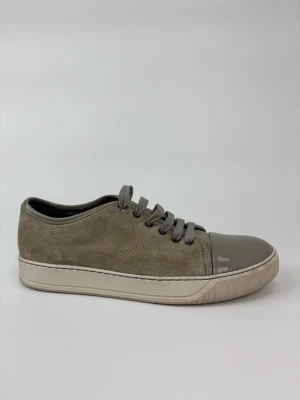 Gråa Lanvin sneakers med mocka och lack - Stilrena sneakers i grå mocka med matchande grå snörning och glansig lackad tå. Snygg kontrast mellan material och en klassisk låg modell som passar till många outfits. Sulan är ljusbeige och ger en fräsch look.