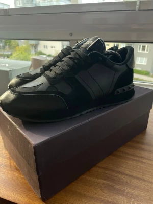 Valentino Rockrunners - Snygga helsvarta sneakers från Valentino med detaljer i både läder och mocka. Skorna har svarta nitar på hälen och en klassisk låg siluett. Perfekta för dig som gillar stilrena och exklusiva sneakers med en edgy touch.