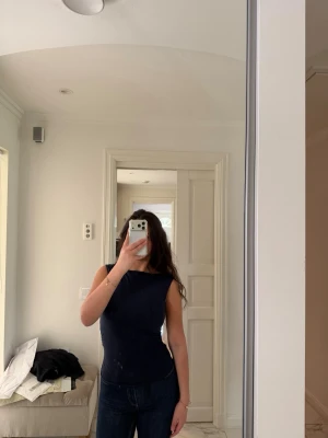 Mörkblå ärmlös topp - Säljer en stilren mörkblå ärmlös topp med rund halsringning. Toppen har en tight passform och är perfekt att matcha med jeans eller kjol. Enkel och clean design utan synliga detaljer eller mönster.