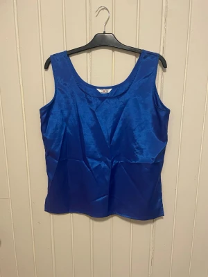 Blå linnetopp från Champagne - Snygg blå linnetopp från Champagne i glansigt material. Toppen är ärmlös med rund halsringning och har en enkel, stilren design som passar perfekt till jeans eller kjol. Perfekt för dig som gillar färg och vill sticka ut lite extra.