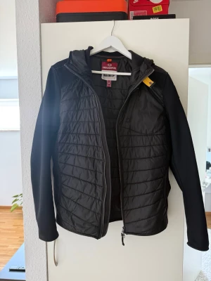 Svart pufferjacka från PARAJUMPERS - Svart pufferjacka från PARAJUMPERS med huva och dragkedja framtill. Jackan har quiltade partier på bröst och rygg samt släta, stretchiga ärmar och sidor. Perfekt för kalla vinterdagar och har en sportig look.