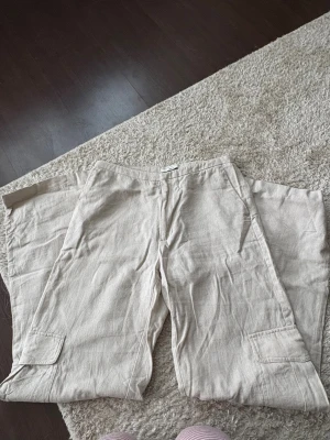 Beiga vida linnebyxor med fickor - Snygga och luftiga beigea linnebyxor med raka, vida ben och sidofickor från Gina tricot. Storlek: XS. Använda några få gånger, skrynkliga pga legat  vikta i garderoben. Kan steamas innan dem skickas iväg. 