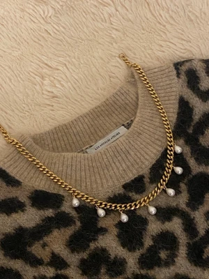 Guldfärgat halsband med pärlor - Snyggt halsband i guldfärgad rostfritt med kedja och sju hängande vita pärlor. Kedjan har en klassisk, chunky design som ger ett trendigt intryck. Perfekt accessoar för att lyfta din outfit med en elegant touch.