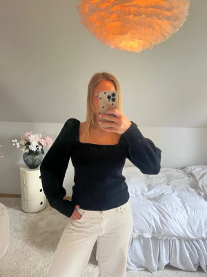 Svart stickad topp med puffärm - Svart stickad topp med fyrkantig ringning och långa puffärmar. Snygg och trendig modell som ger en cool siluett. Perfekt att styla med jeans eller kjol för en modern look.