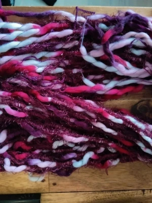 Färgglatt halsduk i röd lila pastellfärger  - Unikt handspunnet garn i tjock och tunn struktur med färger i lila, vinrött, rosa, vitt och rött. Garnet har inslag av glittriga trådar och passar perfekt till kreativa DIY-projekt eller accessoarer. Materialet är en blandning av ull och syntet.