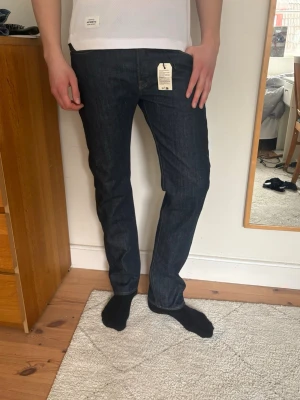 Mörkblå raka jeans från Levi's - Jeansen är helt nya från butik där det ursprungliga priset var 1150. Så här får du de för 250 kr billigare. Mörkblå raka jeans från Levi's med klassisk femficksdesign och knappgylf. Jeansen har en tidlös look och är tillverkade i slitstark denim. Perfekta för dig som gillar en clean och enkel stil.  