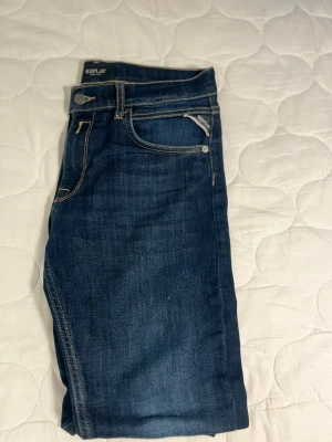 Mörkblå jeans från Replay - Snygga mörkblå jeans från Replay med klassisk femficksmodell och kontrastsömmar. Jeansen har en rak passform och är tillverkade i bomull med en liten mängd elastan för extra komfort. Perfekta för dig som gillar stilrena och tidlösa jeans.