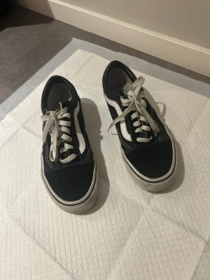 Svarta Vans Old School sneakers - Klassiska Vans sneakers i svart med vit sula och vit sidostripes. Skorna har vita snören och kontrastsömmar. Ovandelen är i canvas och mocka vilket ger en snygg och tidlös look. Använda sparsamt. 