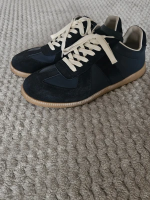 Marinblå Maison Margiela Gats - Snygga marinblå sneakers.. Ovandelen är i en mix av mocka och slätt läder. Säljer dem för jag har ändrat stil lite. Har bara använt de en gång för o testa. Ställ gärna frågor. Ni fattar anledningen till priset.