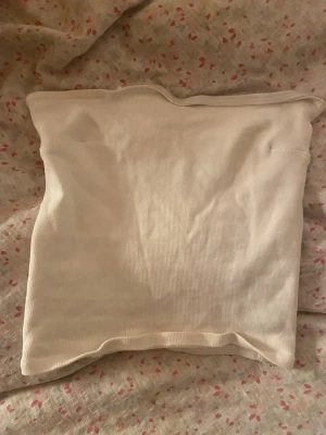 Vit tubtopp - Säljer en enkel och stilren vit ribbad tubtopp från Gina Tricot i storlek XS. Toppen är axelbandslös och har en mjuk, stretchig passform som sitter snyggt på kroppen. Perfekt att matcha med jeans eller kjol för en clean look.