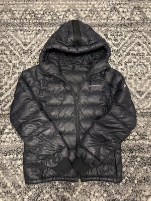 Svart dunjacka från Peak Performance - Snygg svart dunjacka från Peak Performance med huva och dragkedja framtill.  Jackan är i storlek M. Dragkedjan kan vara lite svår att stänga men jag har fått det att funka ganska lätt, lite problem! Hör av er vid eventuella frågor eller funderingar!!