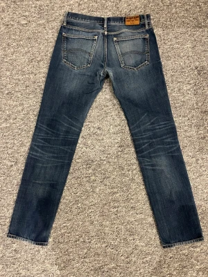 Mörkblå raka jeans från Tommy Hilfiger  - Säljer ett par mörkblå jeans från Tommy hilfiger med raka ben och klassisk femficksmodell. Jeansen har snygga slitningar och är i storlek w31 och L34