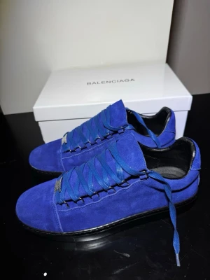 Blåa Balenciaga sneakers i mocka - Snygga blåa sneakers från Balenciaga i mjuk mocka med breda matchande skosnören och svarta detaljer. Låg modell med svart sula och guldfärgad logga på innersulan. Perfekta för dig som vill sticka ut med stilrena och exklusiva skor.