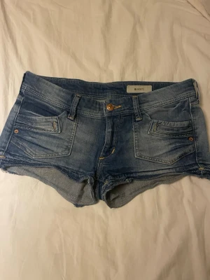 Low waist jeans shorts - Säljer ett par sjukt snygga jeansshorts som sitter lågt i midjan – perfekt för Y2K stil. Modellen framhäver former fint och funkar både till en basic topp eller något mer uppklätt.  Storlek: 36 Midjemått (rakt över): ca 39 cm Passform: Low waist / tight fit Färg: Klassisk blå denim med snygg tvätt  Skick: I mycket fint skick! Lite lätt slitage nertill vid låren (se bild), vilket bara ger den där extra “vintage” känslan.