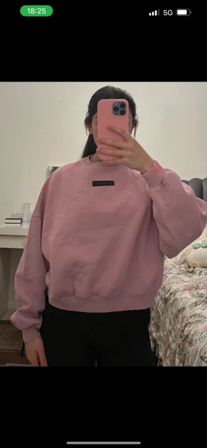 Ljusrosa oversized sweatshirt - En ljusrosa oversized sweatshirt med rund halsringning och ribbade muddar vid ärmslut och nederkant. Tröjan har en liten svart patch med text på bröstet. Tillverkad i mjukt bomullsmaterial, perfekt för en avslappnad och trendig look.