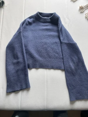 Blå croppad stickad tröja NA-KD - Säljer en blå croppad stickad tröja från NA-KD. Tröjan har långa ärmar, ribbad halsringning och är gjord i ett mjukt material. Perfekt för dig som gillar trendiga och bekväma plagg med avslappnad passform.