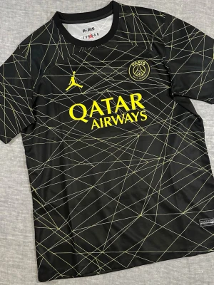 Jordan x PSG Black Yellow Geometric Jersey Qatar Airways Size L Streetwear - Jordan x PSG jersey, black/yellow geometric pattern with Qatar Airways sponsor. Embroidered PSG crest and Jumpman logo. Lightweight polyester performance fabric, athletic fit. Size L. Measurements: P2P 54 cm, waist 53 cm, S2S 44 cm, length 74 cm. Clean football x streetwear crossover piece. Good used condition with normal wear. 
