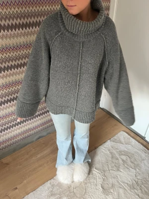 Grå oversized stickad polotröja - Mysig grå stickad polotröja med oversized passform och breda ärmar. Tröjan har en hög, ribbad polokrage och ribbade muddar vid ärmslut och nederkant. Perfekt för kalla dagar och enkel att styla till jeans eller kjol. Något nopprig men den var även det när man köpte så tror lite är meningen