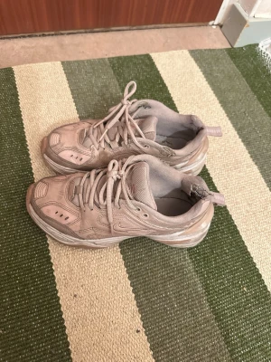 Beige Nike sneakers chunky modell - Chunky sneakers från Nike i beige färg med klassisk swoosh på sidan. Skorna har mesh- och syntetpaneler, vadderad plös och hälflik för enkel påtagning. Snygg retrovibe och passar perfekt till streetwear eller casual outfits.