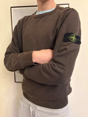 Brun sweatshirt från Stone Island - Säljer en brun sweatshirt från Stone Island med klassisk rund hals och ikonisk logga på vänster ärm. Tröjan har ribbade muddar vid ärmslut och midja, och är gjord i mjuk bomull för en avslappnad look. Priset är inte hugget i sten, skriv vid minsta fundering 