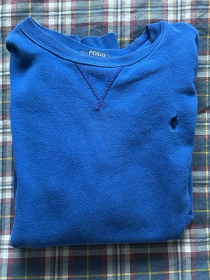 Blå crewneck från Polo Ralph Lauren - Snygg blå crewneck från Polo Ralph Lauren med klassisk rund halsringning och diskret broderad logga på bröstet. Tröjan har ribbade muddar vid ärmslut och nederkant. Perfekt för en avslappnad och stilren look. Sitter baggy, passar runt 170