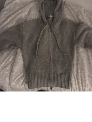 Grå stickad zip hoodie med huva - Mysig grå hoodie från Zara med dragkedja framtill och huva med snören. Tillverkad i mjukt stickat material och har ribbad mudd vid midjan. Perfekt för sticholmstil! Knappt använd. Säljer då den tyvär inte passar. (Inte min bild) 