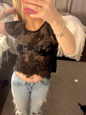 Svart spetsig croppad topp - Säljer en svart topp med vackra spetsdetaljer och korta ärmar. Toppen har ett blommigt mönster i spetsen, lappen är bortklippt men skulle säga xs/s,  pris kan alltid diskuteras💕