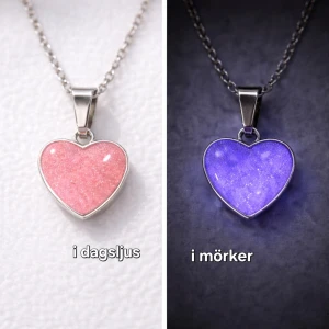 Halsband med hjärthänge som lyser - Snyggt halsband med ett hjärtformat hänge i rosa som skimrar i ljuset och lyser svagt lila i mörkret. Kedjan är i silverfärgad rostfritt stål och hänget har en slät, glansig yta. Perfekt för dig som gillar unika detaljer och vill sticka ut lite extra. Hänget är handgjort och arbetat i lager samt monterat på kedja. Vanligt dagsljus räcker för att hänget ska ändra färg till lila i mörkare omgivning. Kedjan är 45 cm i rostfritt stål. (Tål vatten utan att missfärgas).