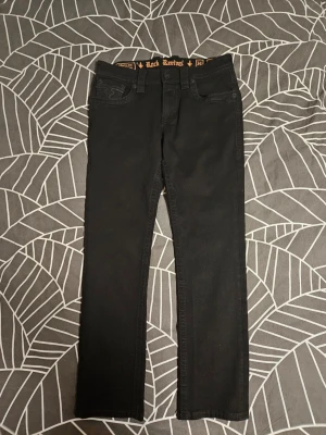 Svarta Jeans från Rock Revival - (Riktiga Rock Revivals, Aldrig använda) Snygga svarta jeans från Rock Revival med raka ben och broderade detaljer på bakfickorna. Klassisk femficksmodell med knappgylf och tydlig logga i midjan. Perfekta för dig som gillar streetwear och vill ha något stilrent men ändå med edge. Pris kan diskuteras. 