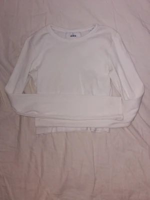 Vit långärmad topp från JXX - En enkel och stilren vit långärmad topp från JXX. Modellen är croppad med rund halsringning och har en tight passform. Perfekt att matcha med jeans eller kjol för en clean look.