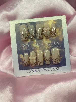 SoftLeo (S);Medium Square;Curved - Snygga handgjorda press-on naglar i beige med brunt leopardmönster och glansig finish. Några naglar har en söt 3D-rosett som detalj. Formen är medium squareform och är en kruvad modell. Perfekt för dig som vill ha ett trendigt och unikt nagelset.S: 15 mm, 11,5 mm, 12 mm, 11 mm, 9 mm 