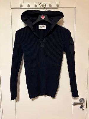 Mörkblå ribbad hoodie/cardigan från HOLEBROOK  - Snygg mörkblå hoodie från holebrook med ribbad struktur och lång ärm. Huva med broderad text 'HBK202' baktill och knappdetaljer vid halsen. Perfekt för dig som gillar en stilren look.