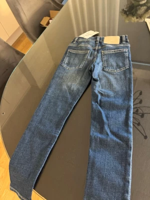 Blå slim fit jeans från Zara - Snygga blå slim fit jeans från Zara med klassisk femficksdesign och läderpatch bak i midjan. Jeansen har en något tvättad look och raka ben. Perfekta för en avslappnad och trendig stil. Materialet är mjukt denim med stretch för extra komfort. Stl 122 6/7 åringar 