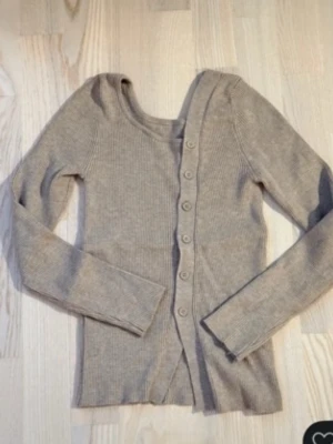 dazy tröja  - Säljer en beige ribbad kofta med långa ärmar och rund halsringning. Koftan har en rak passform och knäppning framtill med matchande knappar. Perfekt att slänga över en t-shirt eller linne för en enkel och stilren look.