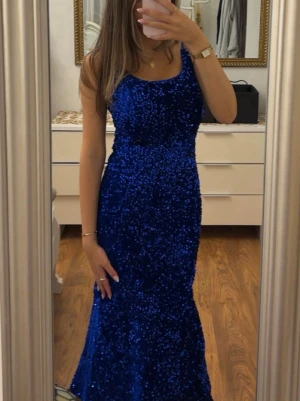 Blå glittrig långklänning - Säljer en blå långklänning täckt av glittriga paljetter. Klänningen har en figurnära passform och är ärmlös med rundad halsringning. Perfekt för dig som vill sticka ut med en elegant och festlig look.