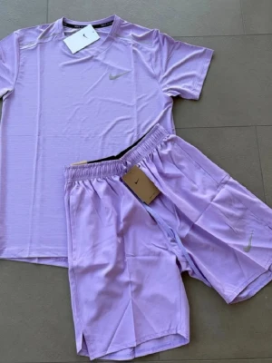 Nike miller - Säljer ett lila träningsset från Nike med t-shirt och shorts. Båda plaggen har diskret Nike-logga på bröstet och benet. Materialet är lätt och andas, perfekt för sport och träning. T-shirten har rund hals och korta ärmar, shortsen har elastisk midja. Har mer färger i mitt plick konto.