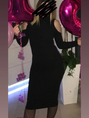 Svart långklänning med cold shoulder - Säljer en svart långklänning med trendiga cold shoulder-detaljer och lång ärm. Klänningen har en kroppsnära passform och hög hals, vilket ger en stilren och modern look. Perfekt för dig som vill sticka ut med en enkel men snygg design.