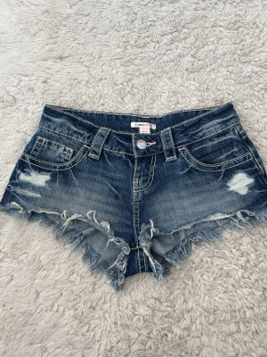 Blå lågmidjade shorts Gina Tricot - Säljer ett par blå jeansshorts från Gina Tricot med slitna detaljer och fransig kant. XXS men är lite för små på mig som bär S. Säljer då de som sagt är för små! 💞