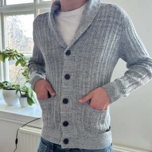 Cardigan grå - Säljer en stilren grå stickad cardigan med knappar framtill och två praktiska fickor. Passar både till jeans och mer uppklädda tillfällen.