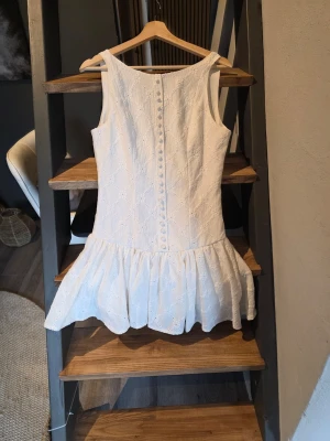 Vit kort Adoore inspirerad klänning med volang - Söt vit kortklänning med broderade detaljer och volang nedtill. Klänningen är ärmlös och har knappar längs ryggen för en extra fin touch. Perfekt för sommarens alla tillfällen och har en lätt, luftig känsla. Från Shein