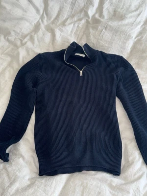 Mörkblå stickad tröja från Zara - Mörkblå stickad tröja från Zara med halv dragkedja och hög krage. Tröjan har ribbstickad struktur, långa ärmar och en klassisk, avslappnad passform. Perfekt för lager på lager och enkel att matcha med jeans eller kjol.