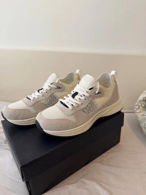 Vita och beige sneakers i mesh och mocka  - Snygga sneakers i vitt och beige med ovandel i mesh och mockadetaljer. Skorna har vita snören, diskret mönster på sidan och en bekväm, tjock sula. Perfekta för en clean och stilren look till vardagsoutfiten.