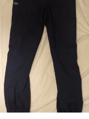 Mörkblå mjukisbyxor från Lacoste - Mörkblå mjukisbyxor från Lacoste med klassisk logga på höften. Perfekta för en avslappnad och sportig stil. Tillverkade i mjukt material för extra komfort.
