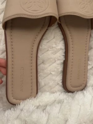 Beige sandaler från Anna Field - Snygga beige sandaler från Anna Field med öppen tå och bred rem framtill. Sandalerna har en platt sula i brunt och är tillverkade i syntetmaterial. Perfekta för en avslappnad och trendig look under varma dagar.