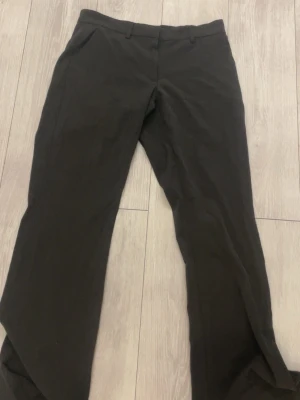 Svarta kostymbyxor med raka ben - Snygga mörkgråa kostymbyxor med stil bootcut och klassisk passform. Byxorna har hällor för skärp och sidofickor. Perfekta för en clean och stilren look. Materialet ser ut att vara en mjuk och lite stretchig blandning.