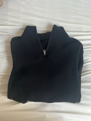 Svart stickad tröja med halvzip - Säljer en svart stickad tröja med hög krage och halv dragkedja framtill. Tröjan har en ribbad struktur och är perfekt för lager på lager. Passar dig som gillar en clean och stilren look. no brand tror jag 
