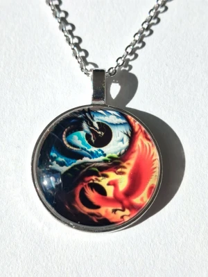 Yin Yang halsband med drakar - halsband med runt hänge i metall och 2D, motiv av två drakar i yin yang-stil. Ena draken är blå och svart, den andra röd och orange, vilket ger en cool kontrast. Kedjan är silverfärgad rostfritt stål och har en klassisk länkdesign i ankarlänk.