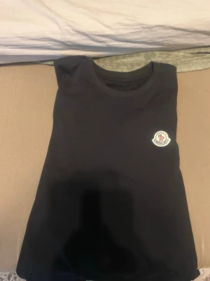 Svart Moncler t-shirt med logga - Snygg svart t-shirt från Moncler med klassisk rund hals och Moncler-logga broderad på bröstet. Enkel och stilren design som passar perfekt till jeans eller shorts. Tillverkad i mjuk bomull för skön känsla hela dagen.