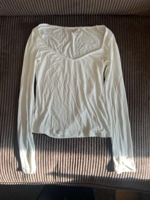 Vit långärmad topp från Nelly - Säljer en enkel och stilren vit långärmad topp från Nelly. Toppen har en v-ringad hals med spetskant och är tillverkad i mjuk bomull. Perfekt att matcha med jeans eller kjol för en clean look.